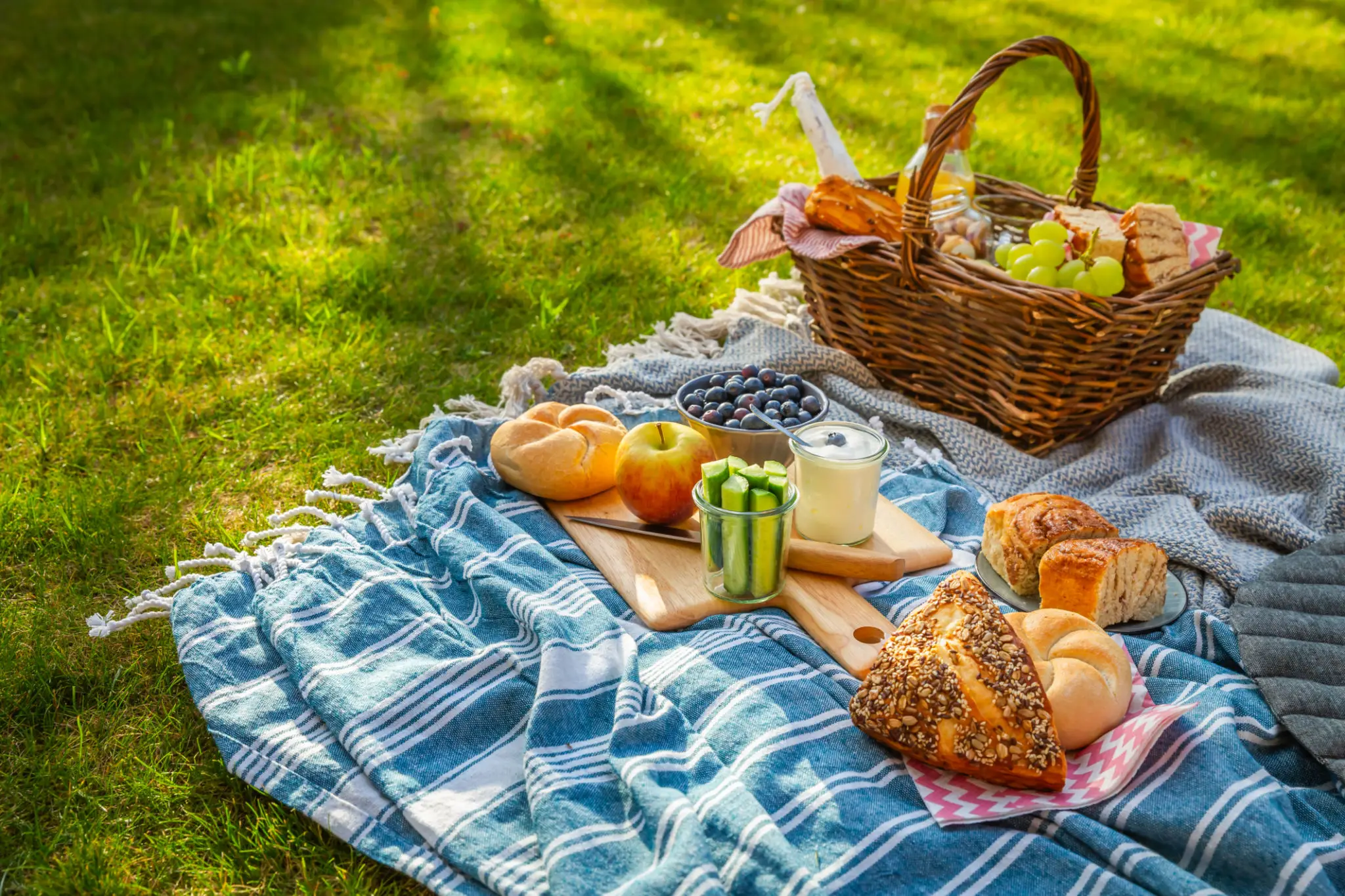Picnic spread with basket, bread, fruit on blanket